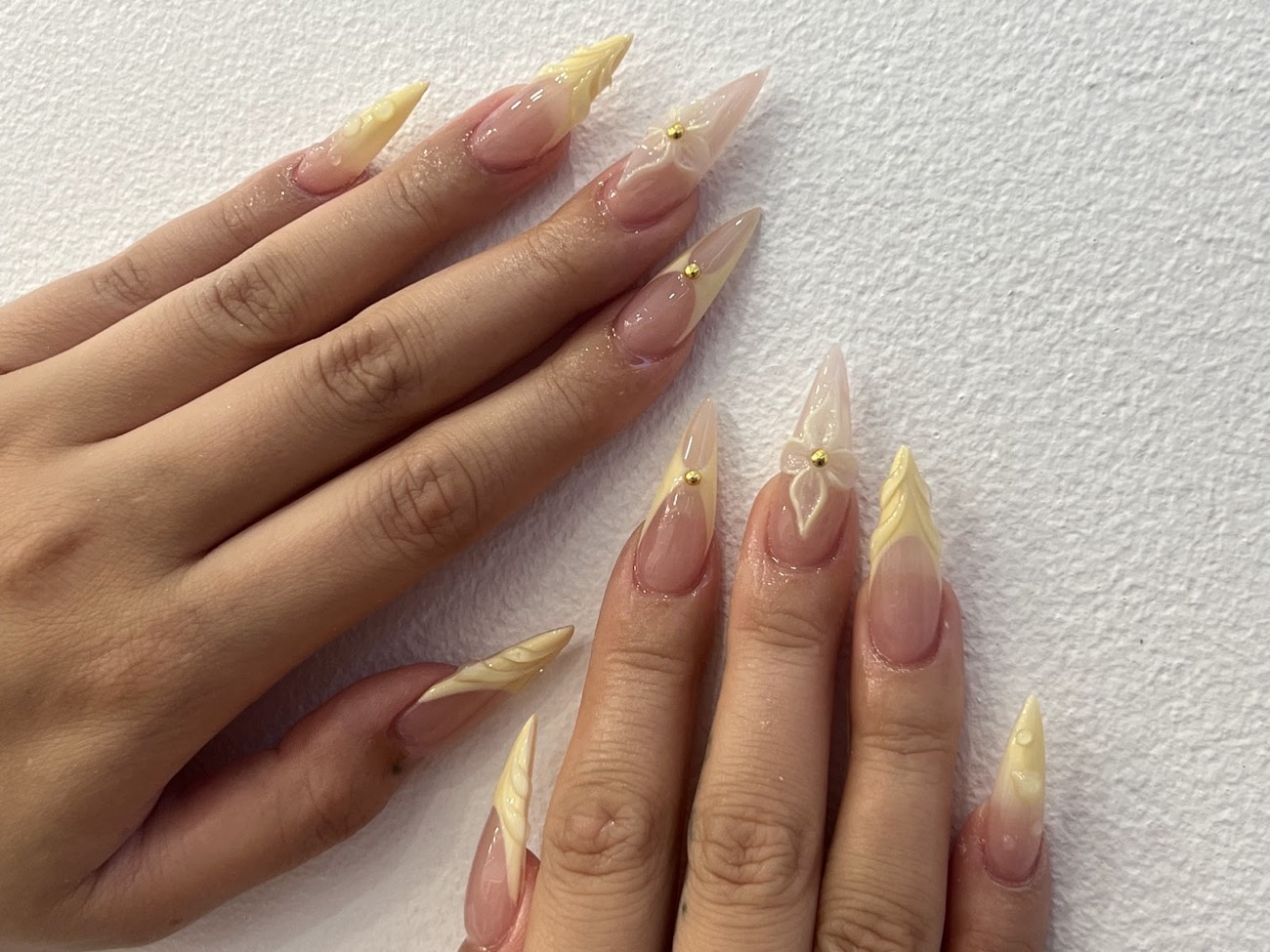 Long stiletto nails in a buttery pastel yellow with sculpted 3D flowers and gold detail